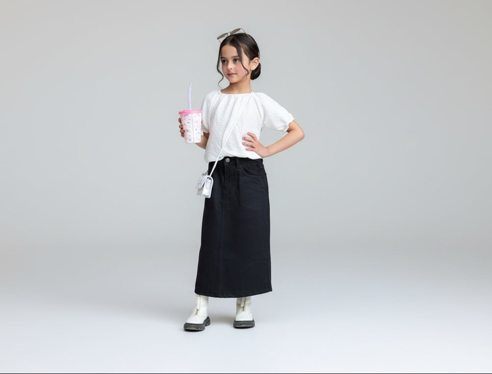 Person wearing a white shirt and black skirt holding a pink drink on a plain background
